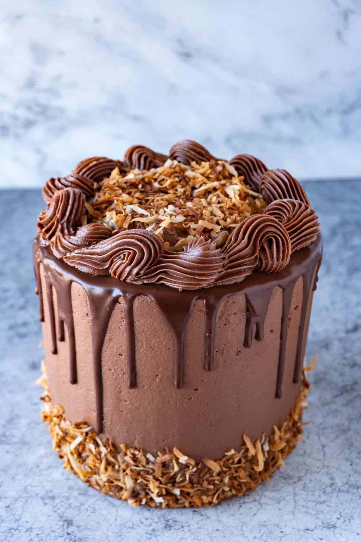 German Chocolate Cake side view decorated with chocolate drip, toasted coconut and piped frosting